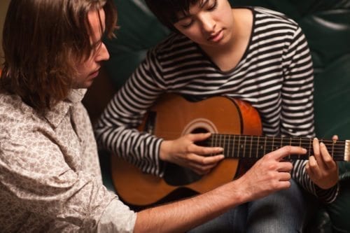 Young Musician Teaches Female Student To Play The Guitar.